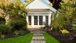 A cute white house with a lush green back yard lined with pavers.