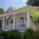Historical home with Texas flags adorning the posts on the front porch with woman standing next to them.