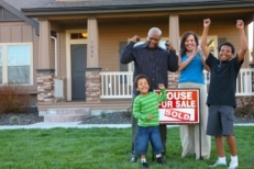 Family cheering in front of new house next to a for sold sign.