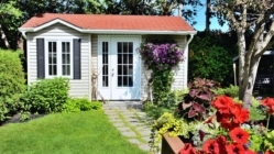 A small garden ADU in a backyard with grass and flowers in front of it