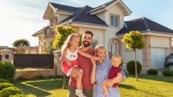 Family buying a new house; parents and children hugging and having fun standing in front of their new house