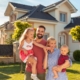 Family buying a new house; parents and children hugging and having fun standing in front of their new house