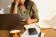 A stressed person sitting at a table with a credit card, laptop, and a cell phone