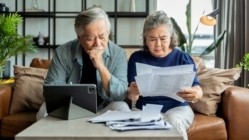 Older retired Asian senior couple checking and calculate financial billing together on sofa involved in financial paperwork