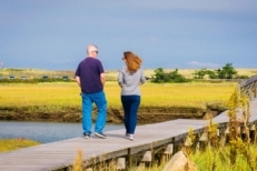 A couple enjoys the early October weather as they have a conversation walking along the iconic Sandwich Boardwalk that crosses Mill Creek and the salt marsh and leads tp Town Neck Beach