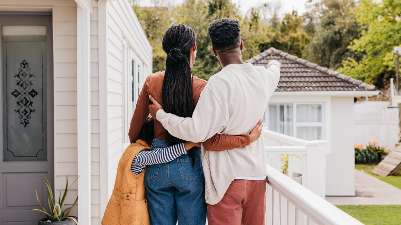 Couple with daughter hugging each other, standing on terrace of new home, pointing and looking into distance