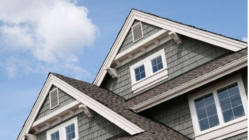 Top of a house with gray siding and white windows against a blue sky
