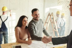 A couple working on a renovation project, with the help of the construction crew, shaking the hands of the Loan Lender.