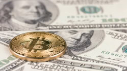 A representation of a Bitcoin on top of several US Dollar bills