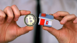Agent holding a representation of a Bitcoin and a home indicating how to buy a home with Bitcoin