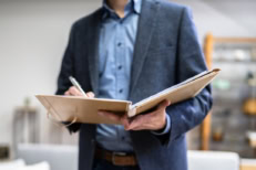 An appraiser in a suit holding a clipboard in front of them in a house