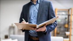An appraiser in a suit holding a clipboard in front of them in a house