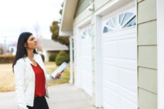A real estate appraiser standing in front of a garage holding a clipboard.