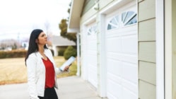 A real estate appraiser standing in front of a garage holding a clipboard.