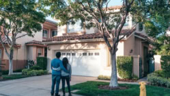 Young couple standing outside their new suburban home, symbolizing first-time homebuyers and real estate ownership in the United States