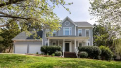 Modern two-story suburban home with gray siding, white trim, and double garage surrounded by trees and a green lawn — perfect example of residential real estate and homeownership.