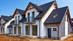 Newly built modern townhouse with black roof tiles, large windows, and small balconies at a residential construction site.