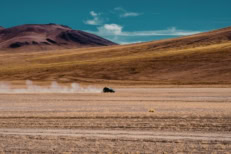 Off-road vehicle driving across a vast desert landscape with mountains in the background, symbolizing long journeys, risk, resilience, and navigating uncertainty.