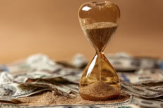 Hourglass sitting on U.S. dollar bills symbolizing the rising cost of waiting, interest rates, inflation, and mortgage timing.