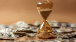 Hourglass sitting on U.S. dollar bills symbolizing the rising cost of waiting, interest rates, inflation, and mortgage timing.