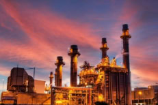 Industrial power plant with gas turbines and smokestacks operating at sunset, representing global energy production, electricity generation, and economic infrastructure.
