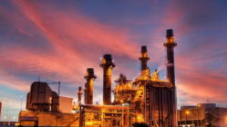 Industrial power plant with gas turbines and smokestacks operating at sunset, representing global energy production, electricity generation, and economic infrastructure.