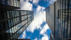 Looking up at modern glass skyscrapers with blue sky and clouds, representing urban architecture and city skyline.