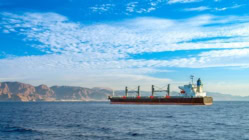 Cargo ship transporting goods across open sea with mountains in the background, symbolizing global trade, oil shipping routes, and economic impact on inflation and interest rates