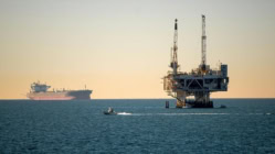 Offshore oil drilling platform in the ocean with tanker ship in the background at sunset, illustrating global oil production, energy markets, and the impact of oil prices on inflation and interest rates.