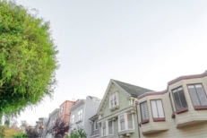 Low angle view of a sloped row of houses in the suburbs There are trees on the left side at the front of the houses on the left with painted wood sidings.