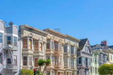Townhouses neighborhood exterior with a view of traffic lights and trees at the front. Neighborhood in San Francisco, California with bow windows and pastel color exterior.