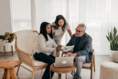 A couple reviews mortgage paperwork with their loan advisor in a sunlit living room.