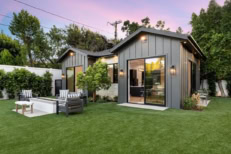 Modern backyard with a small house, ADU, patio furniture, and lush green lawn at sunset.