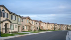 Tree-lined suburban street lined with identical townhouses and row houses in new residential development. Image illustrates housing market, real estate investment, and suburban growth trends relevant to financial and editorial coverage.