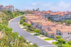 Mountain residential area at Laguna Niguel in California with asphalt road. There are single-family homes on the right beside the road and complex buildings on top of the slope and at the back.