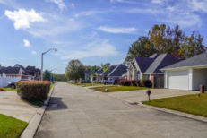 American suburban neighborhood in Baton Rouge with single-story homes, green lawns, parked SUVs and pickup trucks, and a sunny idyllic atmosphere.