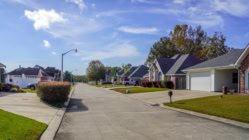 American suburban neighborhood in Baton Rouge with single-story homes, green lawns, parked SUVs and pickup trucks, and a sunny idyllic atmosphere.
